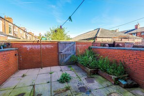 A brick wall with a metal gate, a concrete patio, and some vegetation.