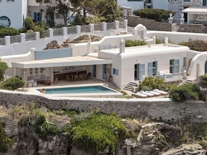 Eine weiße Villa mit Swimmingpool, Sitzgelegenheiten im Freien und einer steinernen Stützmauer.
