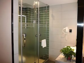 Un baño moderno con ducha de vidrio, lavamanos blanco y una planta en maceta.