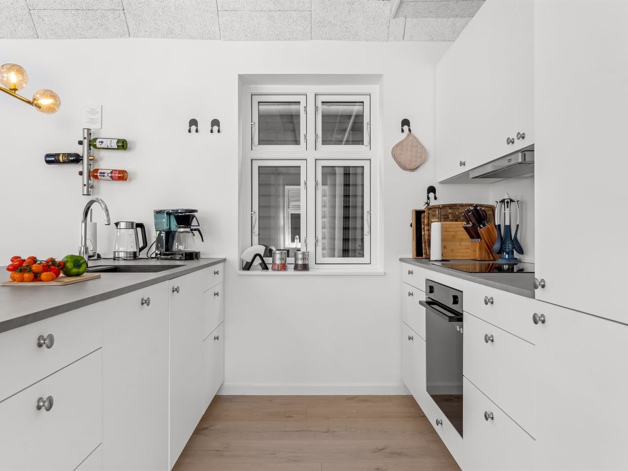 A modern kitchen with white cabinetry, a built-in oven, and a window with blinds.