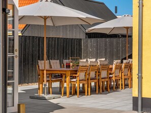 Eine Terrasse im Freien mit einem Holztisch und Stühlen, umgeben von Sonnenschirmen.