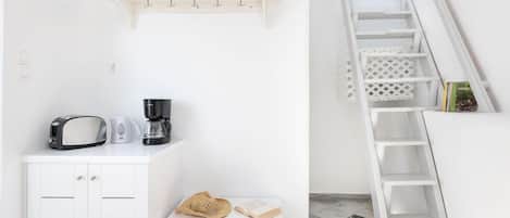 Cuina blanca amb torradora, cafetera i taula petita amb un barret i un llibre.