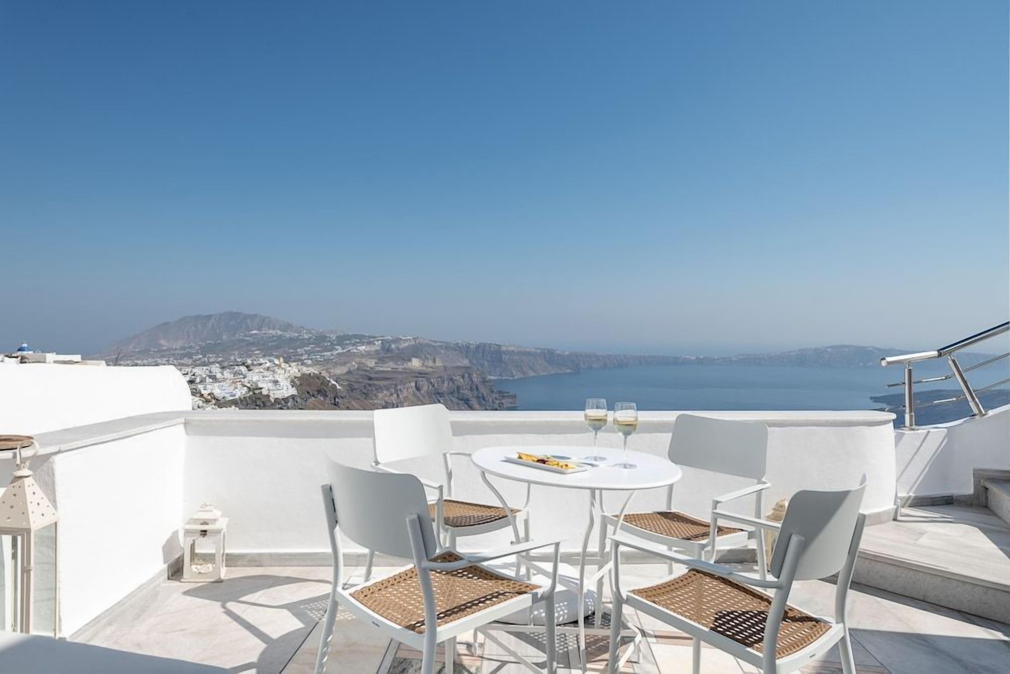Eine Terrasse mit weißer Möbel, ein Tisch mit zwei Gläsern und Blick auf eine Küstenlandschaft.