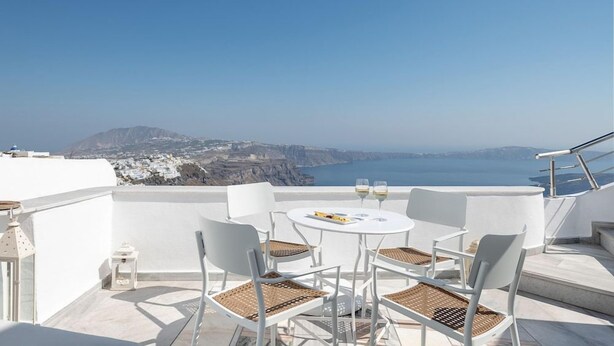 A terrace with white furniture and a table, overlooking a coastal landscape. - Veranda View (Santorini)
