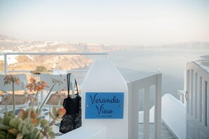 A balcony with a sign reading 'Veranda View,' a table with chairs, a hat, and a black bag. - Veranda View (Santorini)