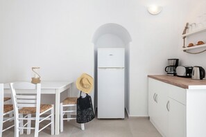 A compact kitchen with a white refrigerator, a dining table with chairs, and a coffee maker. - Veranda View (Santorini)