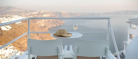 Ein Balkon mit zwei weißen Stühlen, einem Tisch, einem Hut und einem Weinglas.