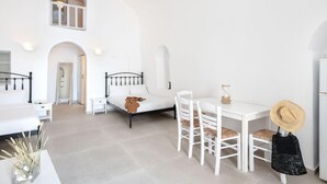 A bright, white interior with a bed, a dining table with chairs, and a small kitchen area. - Veranda View (Santorini)