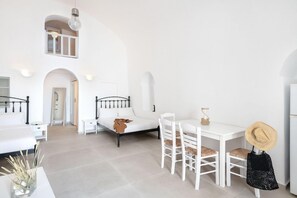A bright, white interior with a bed, a dining table with chairs, and a small kitchen area. - Veranda View (Santorini)