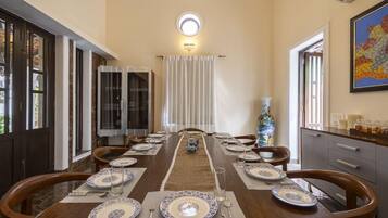 A dining room with a long table set for a meal, a vase, and a painting on the wall.