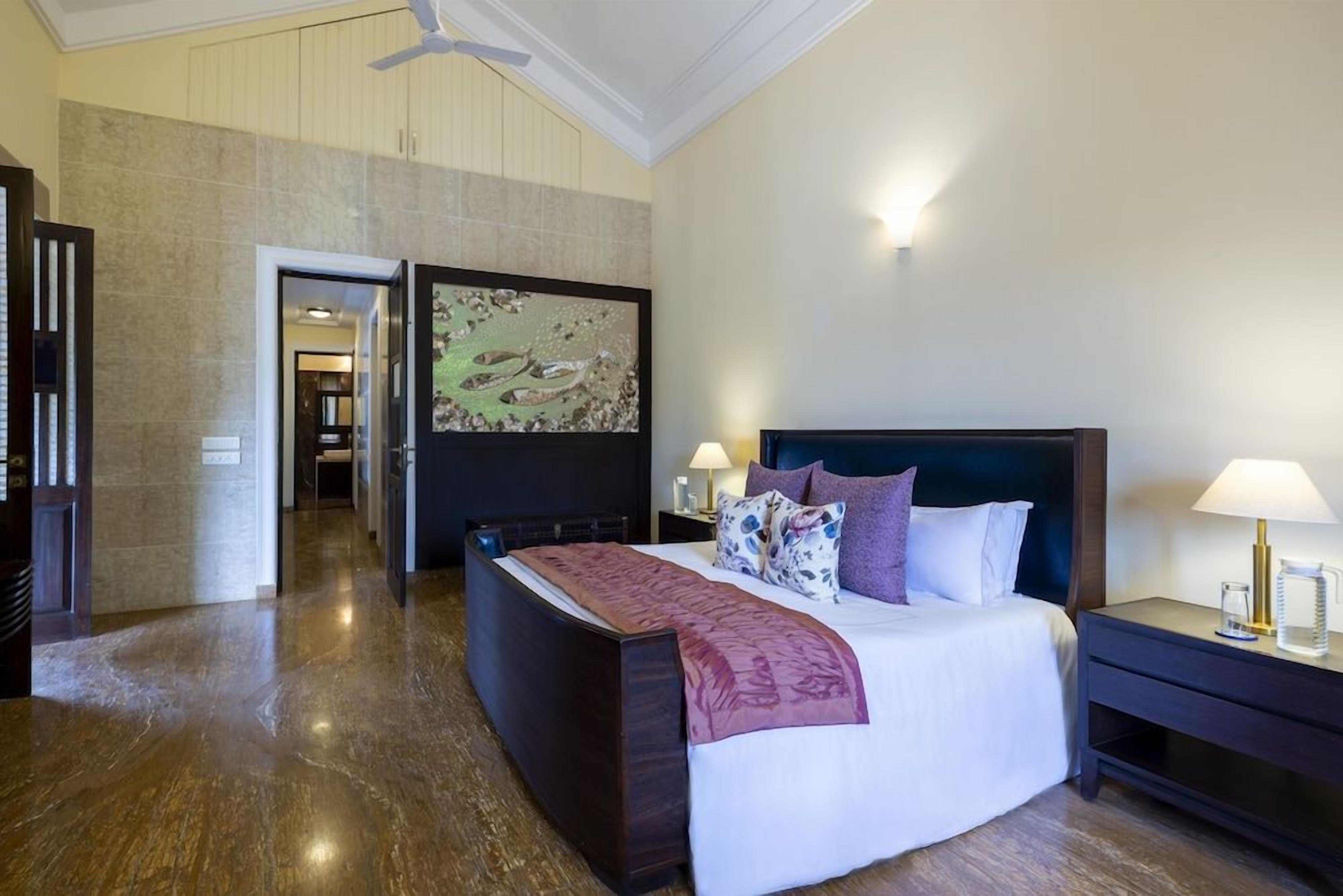 A hotel room with a large bed, a nightstand, a wall-mounted artwork, and a door leading to another room.