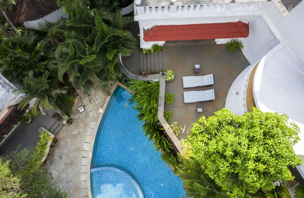 Una vista aerea di un hotel con piscina, poltrone da relax bianche e vegetazione lussureggiante.