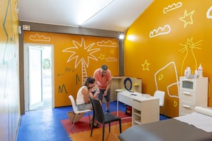 Una habitación con una cama, un escritorio, una silla y una persona adulta junto a un niño.