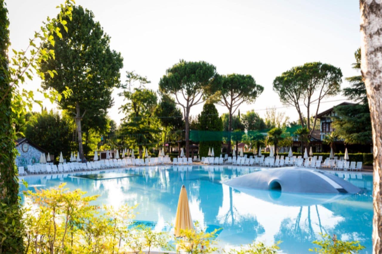 A swimming pool with lounge chairs and umbrellas, surrounded by trees and a building.