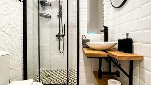 Um banheiro moderno com chuveiro em box de vidro, toucador de madeira e parede revestida de azulejos brancos.