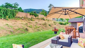 An outdoor patio area with wicker furniture, a large umbrella, and a view of a hilly landscape. - Innhale Cannabis Friendly B&B - Adults Only (Manitou Springs)