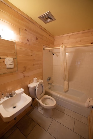 A bathroom with wooden paneling, a sink, toilet, and a bathtub. - The Welcome Inn (Mackinaw City)