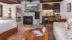 A modern living room with a fireplace, a television mounted on a stone wall, and a dining area with wooden furniture. - Willows, a Destination by Hyatt Residence (Snowmass Village)