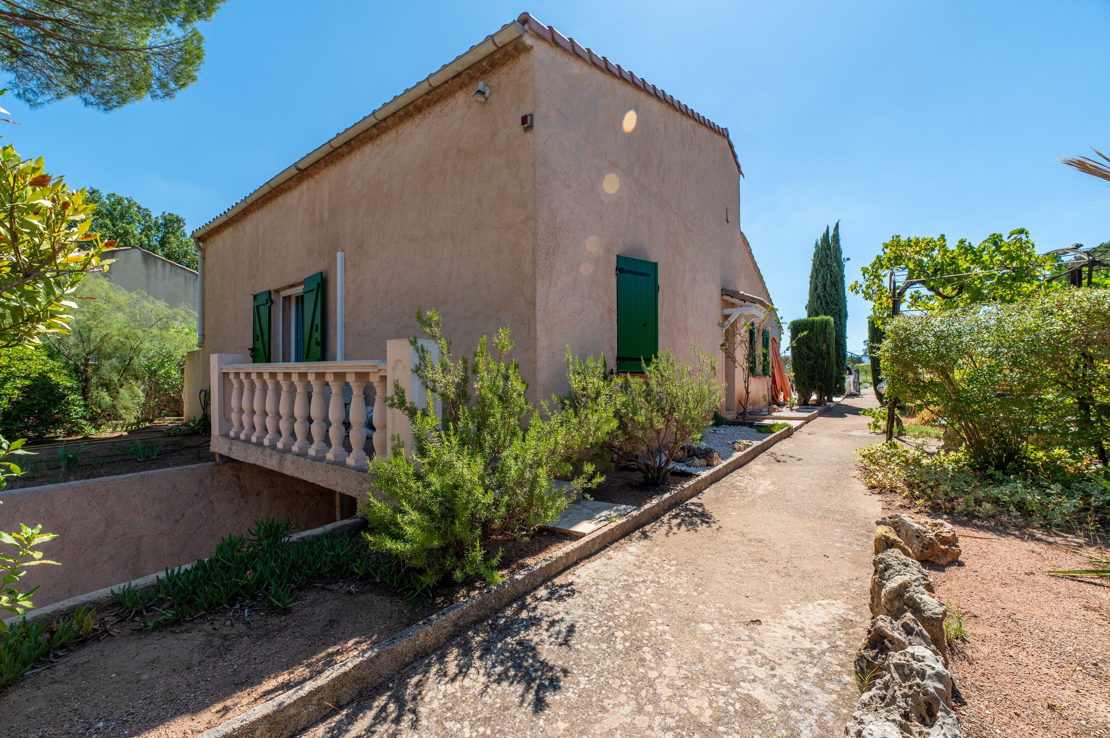 Un bâtiment de style rustique doté d’un balcon, entouré de verdure et bordé d’un chemin de gravier.
