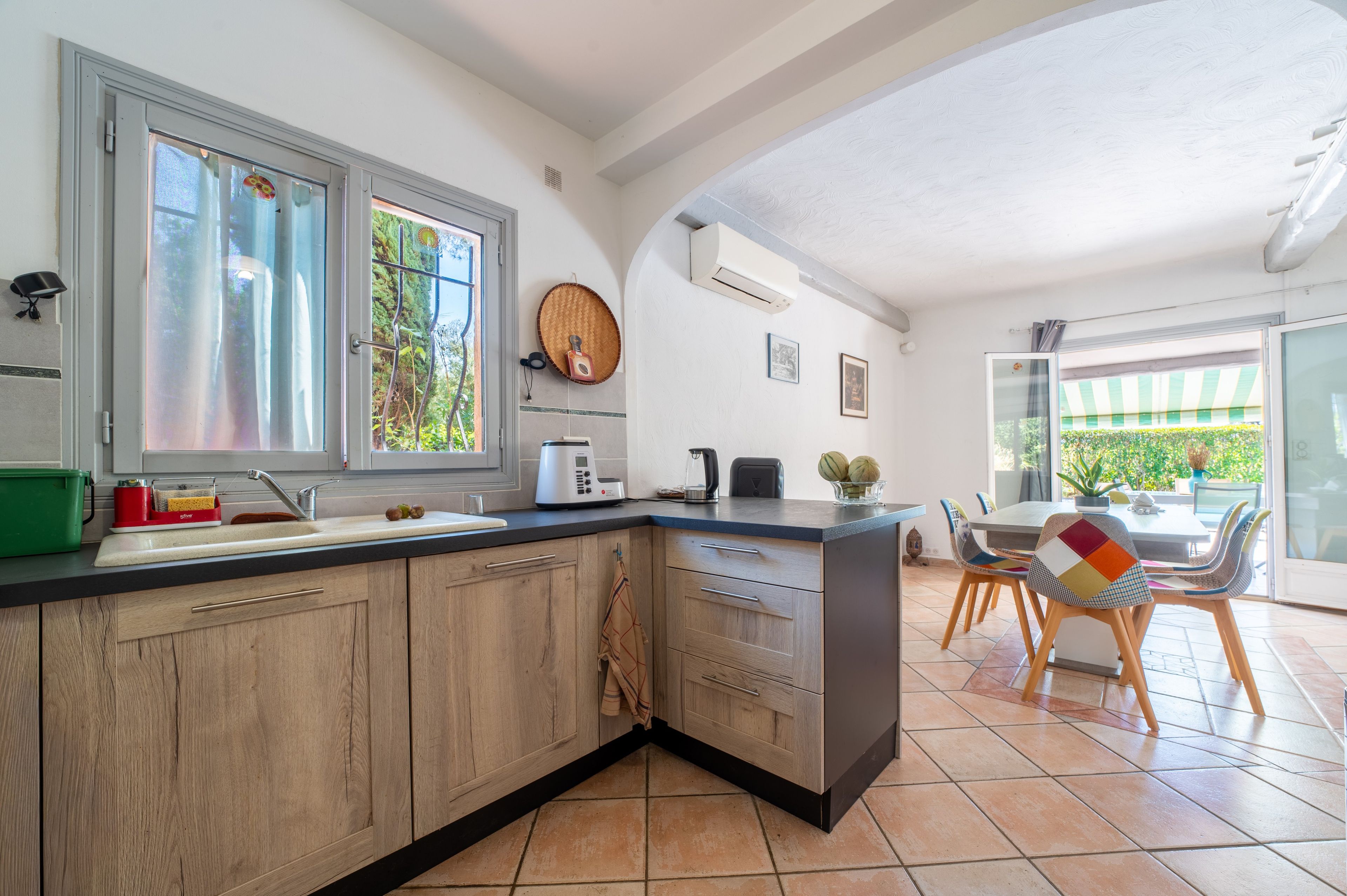 Une cuisine moderne dotée d’un îlot central intégré, d’un coin repas avec une table et des chaises, et offrant une vue sur l’extérieur grâce à une porte-fenêtre coulissante.