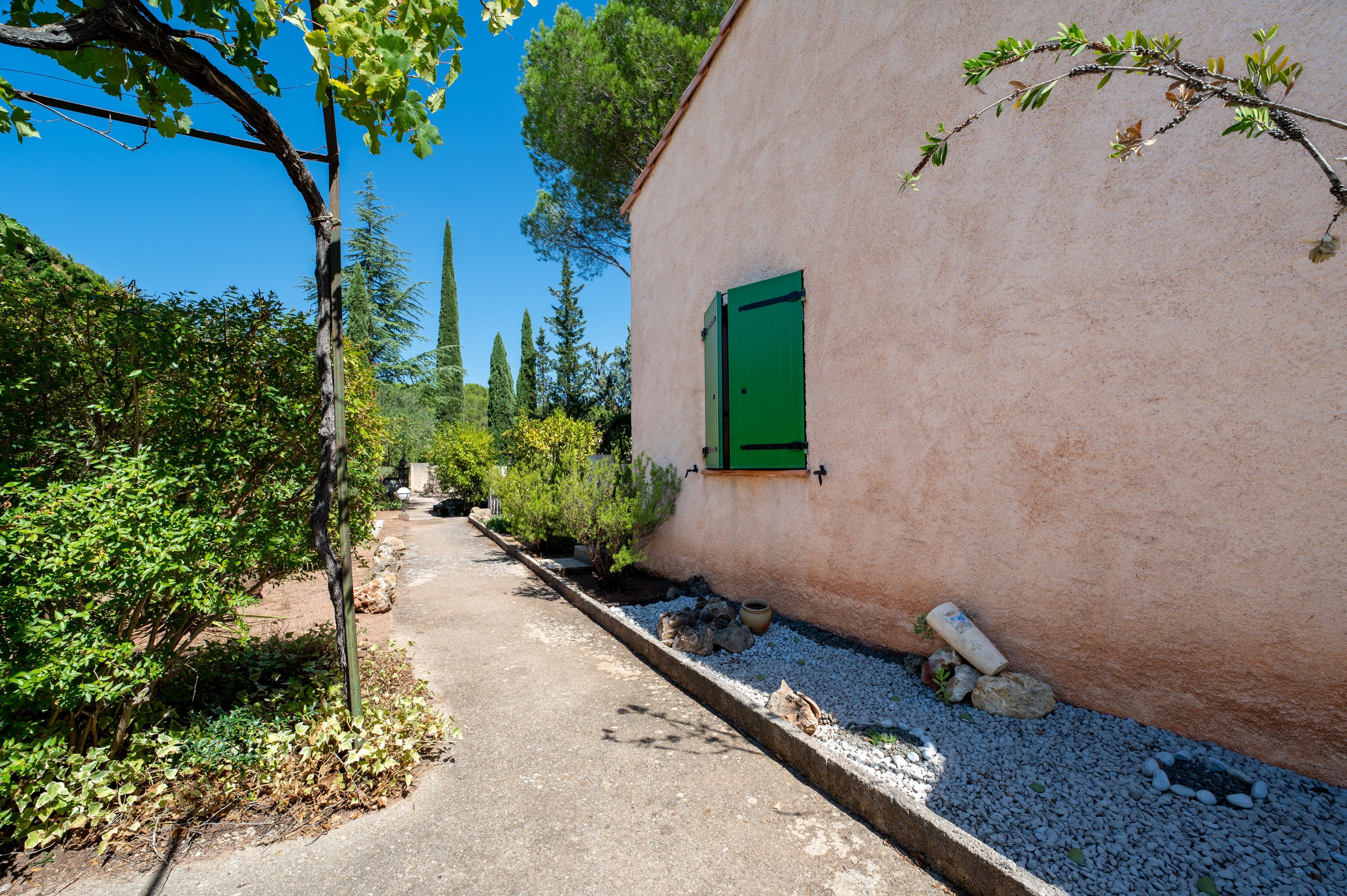 A narrow pathway leading to a building with a green shuttered window.