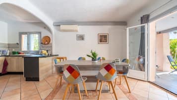 A modern kitchen with a dining area, featuring a large island, chairs with colorful cushions, and a sliding glass door leading to an outdoor area.