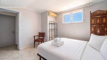 A bedroom with a bed, a chair, a window, and an air conditioning unit.
