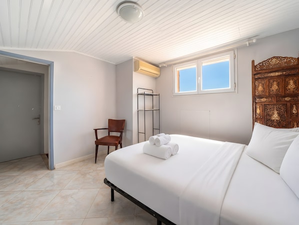 A bedroom with a bed, a chair, a window, and an air conditioning unit.