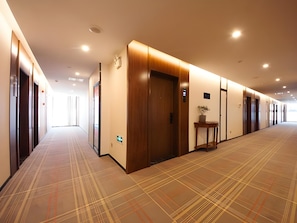 A hotel corridor with multiple doors, a reception area, and a patterned carpet.