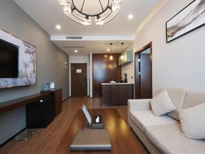 A modern living room with a sofa, a coffee table, a TV, and a kitchen area in the background.