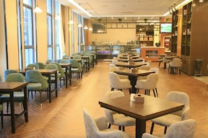 Un restaurant spacieux, doté de nombreuses tables et chaises, d’un bar et de grandes fenêtres laissant entrer la lumière naturelle.