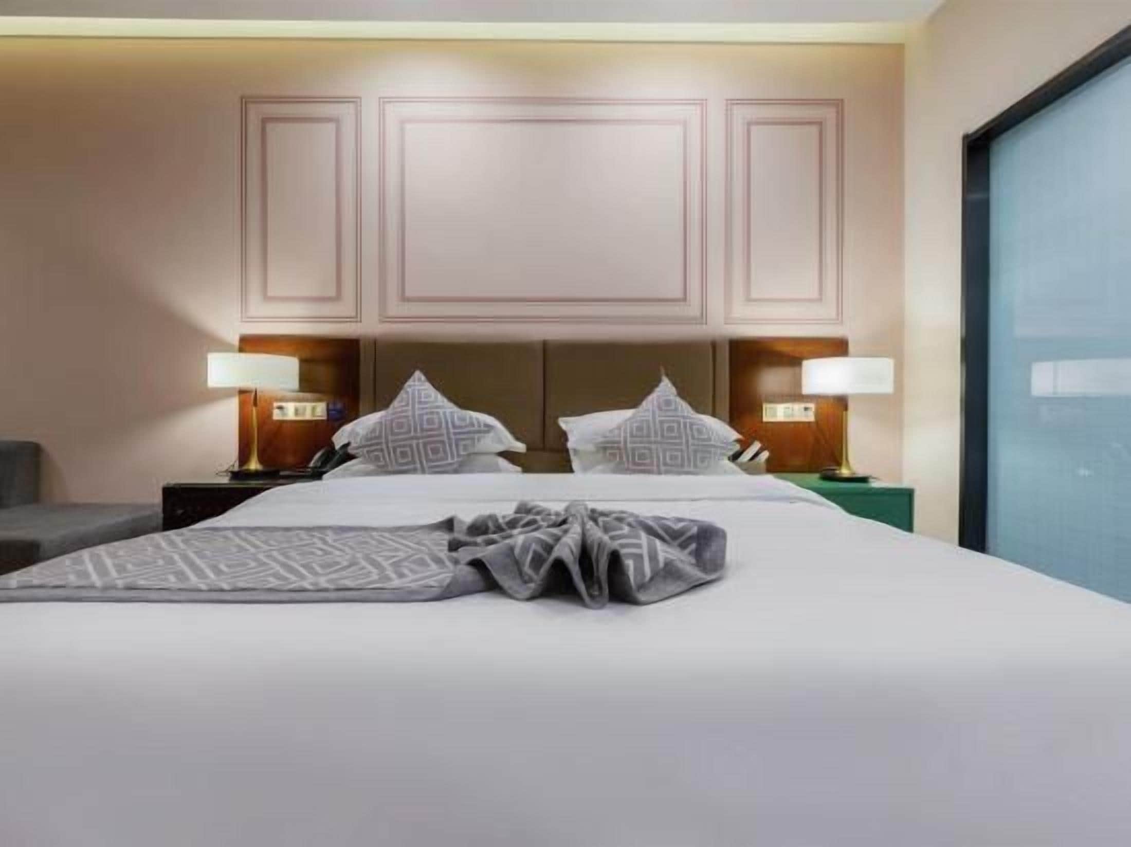 A hotel room with a large bed, two bedside tables with lamps, a headboard, and a window.