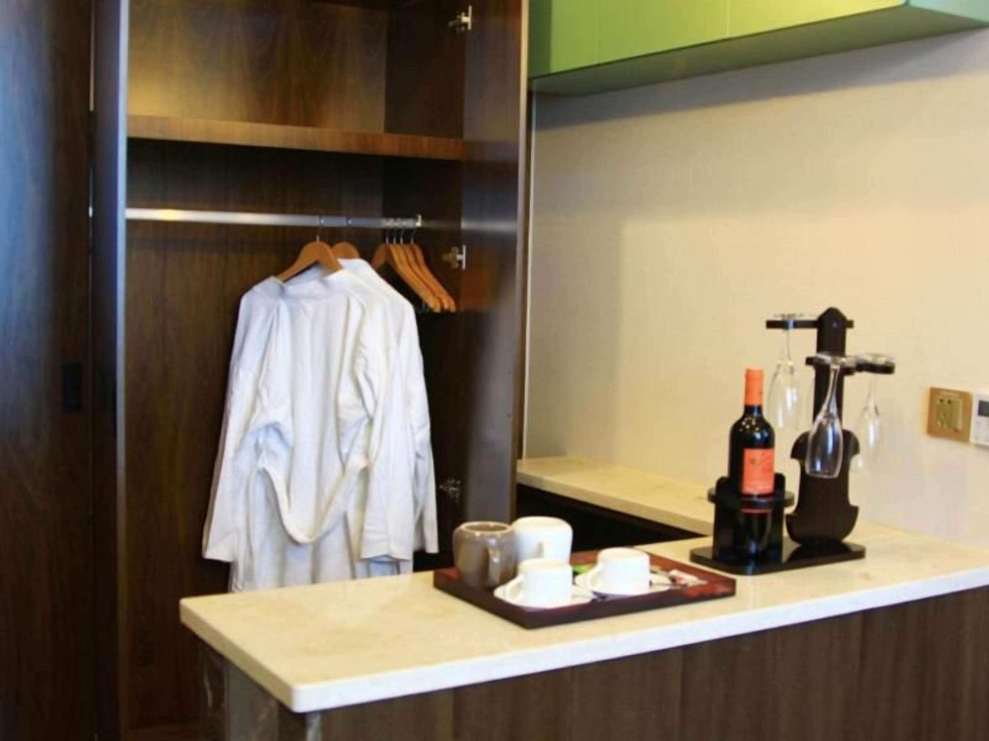 A hotel room with a wooden wardrobe, a minibar with a bottle and glasses, and a counter with a tray of items.
