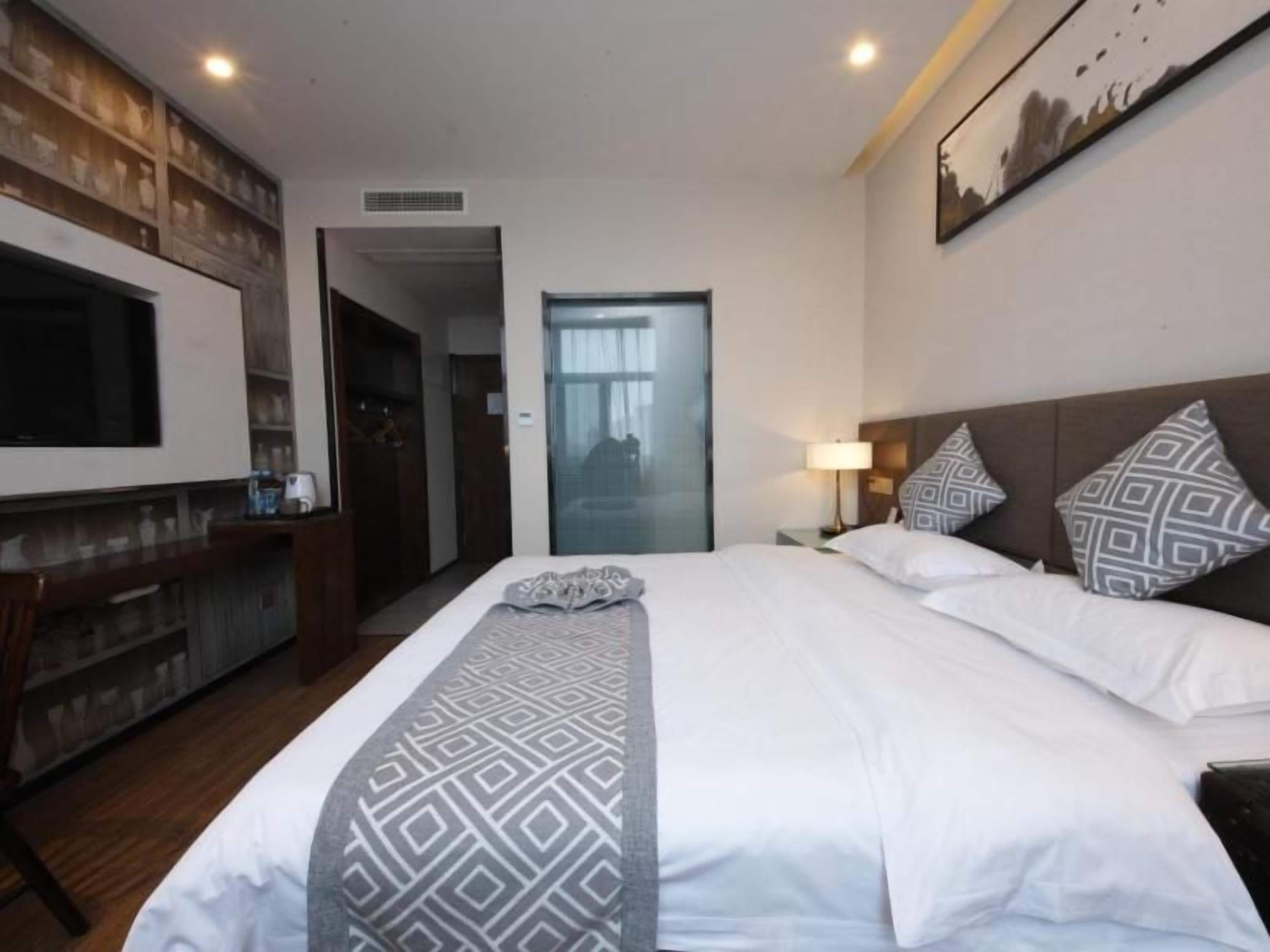 A hotel room with a large bed, a TV mounted on the wall, a desk, and a door leading to another room.