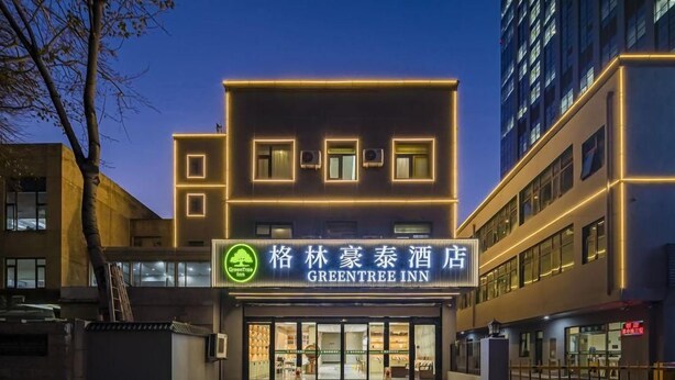 A hotel with a modern facade, illuminated signage, and a gated entrance. - Greentree Inn Tianjin Hexi Olympic Sports Center Cancer Hospital Subway Station Express Hotel (Tianjin)
