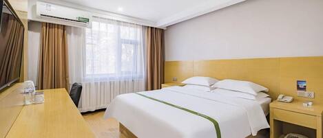 A hotel room with a bed, a desk, a chair, a nightstand, a telephone, and an air conditioning unit.