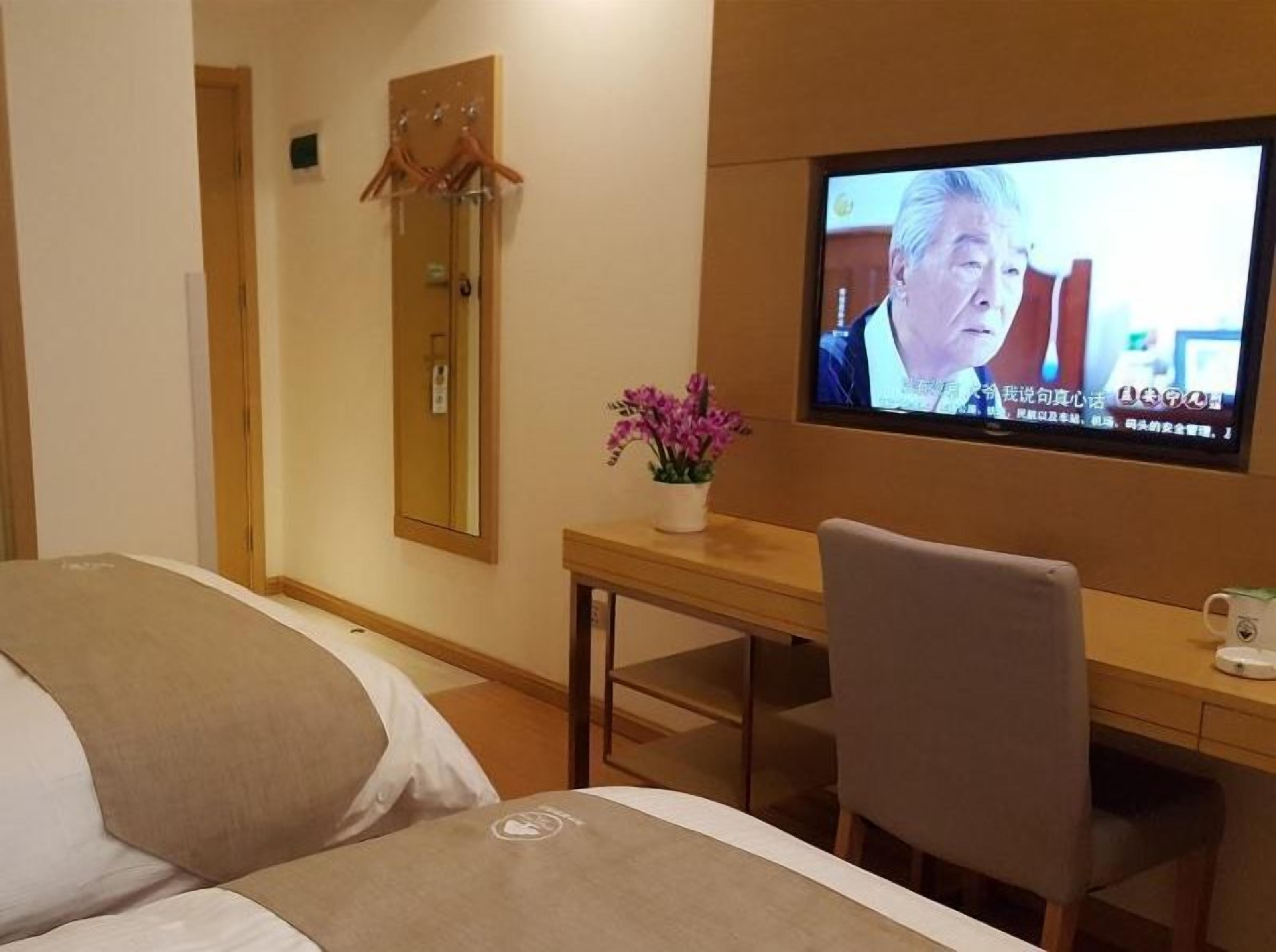 A hotel room with a bed, a desk, a chair, a television, and a mirror.