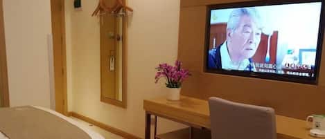 A hotel room with a bed, a desk, a chair, a television, and a mirror.
