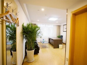 Ein Hotelzimmer mit Holzboden, Schreibtisch, Stuhl, einer großen Topfpflanze und einem Spiegel.