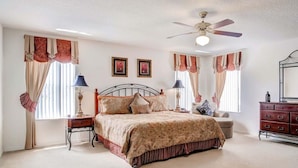 A bedroom with a bed, nightstands, a dresser, a ceiling fan, and curtains. - Sunseeker Villa (Davenport)