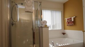 A bathroom with a glass-enclosed shower, a white bathtub, and a window with vertical blinds. - Sunseeker Villa (Davenport)