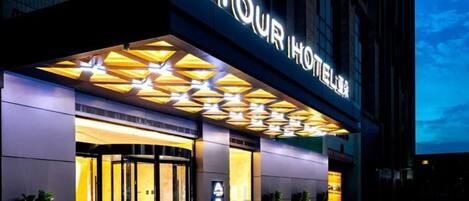 A hotel entrance with a glass door, a neon sign, and a geometric light fixture above.