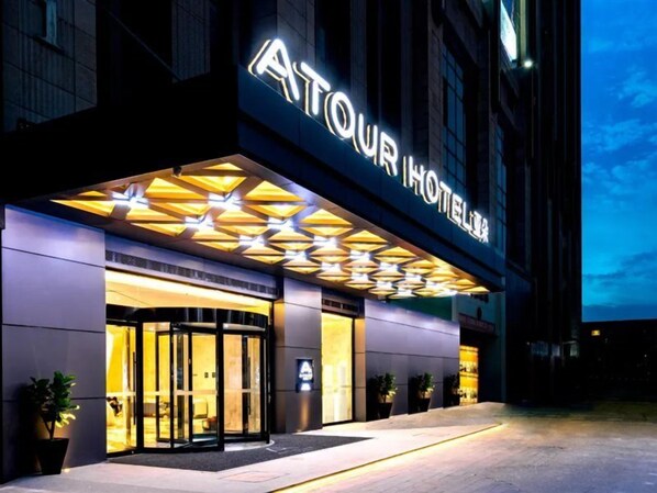 A hotel entrance with a modern design, featuring a prominent illuminated sign and a geometric light fixture above the entrance. - Atour Hotel (Kunming)