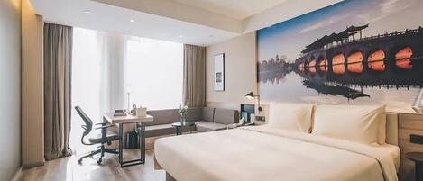 A hotel room with a large bed, a desk, a chair, a sofa, and a painting of a bridge.