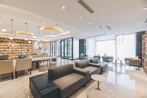 Um saguão de hotel moderno com área de estar, estante de livros e balcão de recepção.
