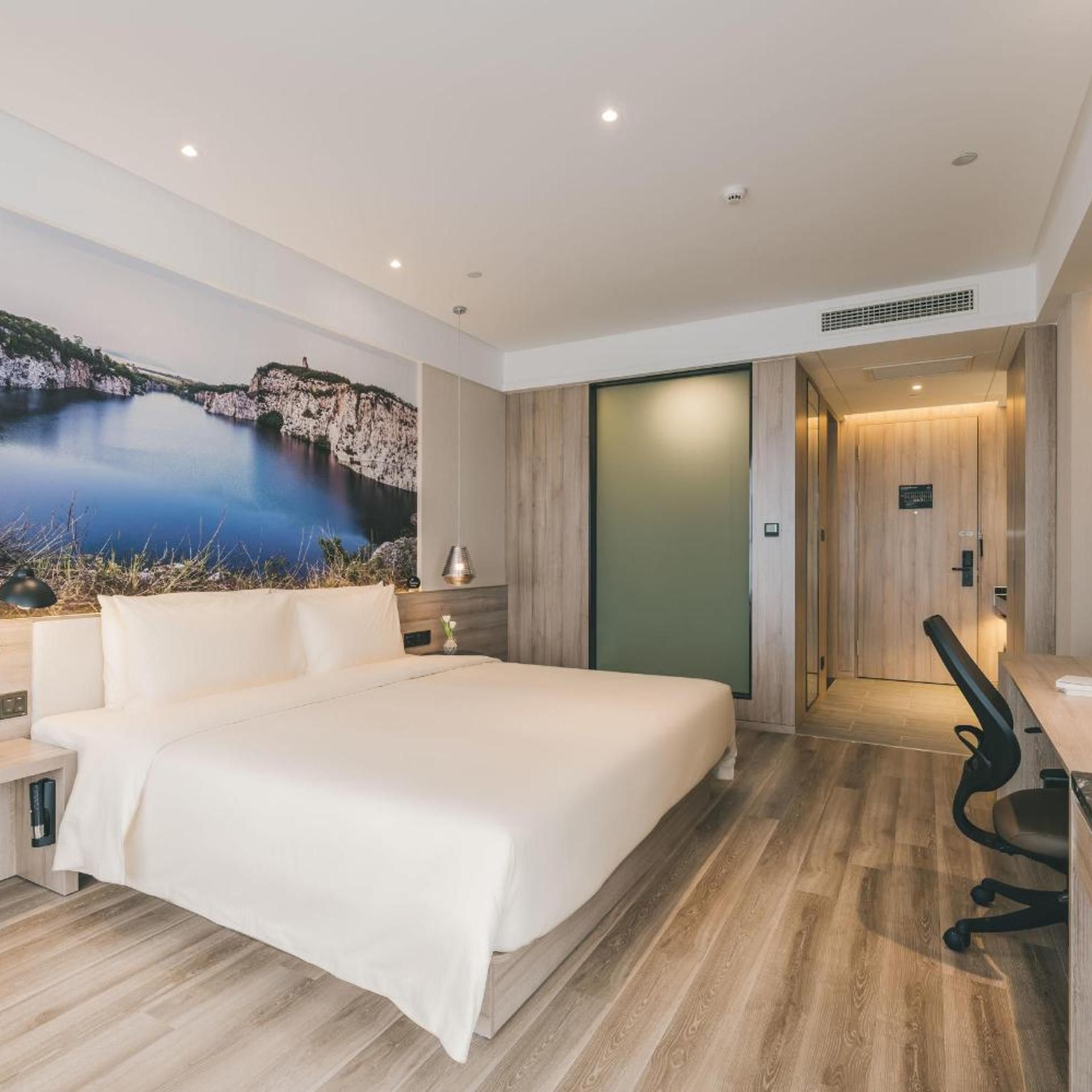 A modern hotel room with a large bed, a desk, and a view of a natural landscape.