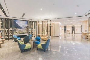 A modern lobby with a large bookshelf, seating area, and a view of a mountainous landscape. - Atour Hotel (Jiaxing)