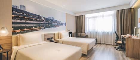 A hotel room with two beds, a desk, a chair, a large window with curtains, and a cityscape mural on the wall.