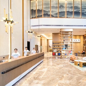 A hotel reception area with a modern design, featuring a reception desk, a staircase, and a seating area with bookshelves. - Atour Hotel (Zhongshan)