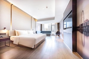 Quarto de hotel moderno com uma cama grande, uma escrivaninha, uma cadeira e vista para a cidade pela janela.